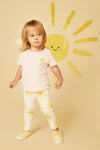 Child wearing a light pink shirt and white pants with yellow sun patterns, standing against a beige background with a yellow sun illustration.