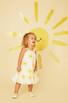 Child wearing a yellow and white dress with floral patterns against a yellow background with a sun design.