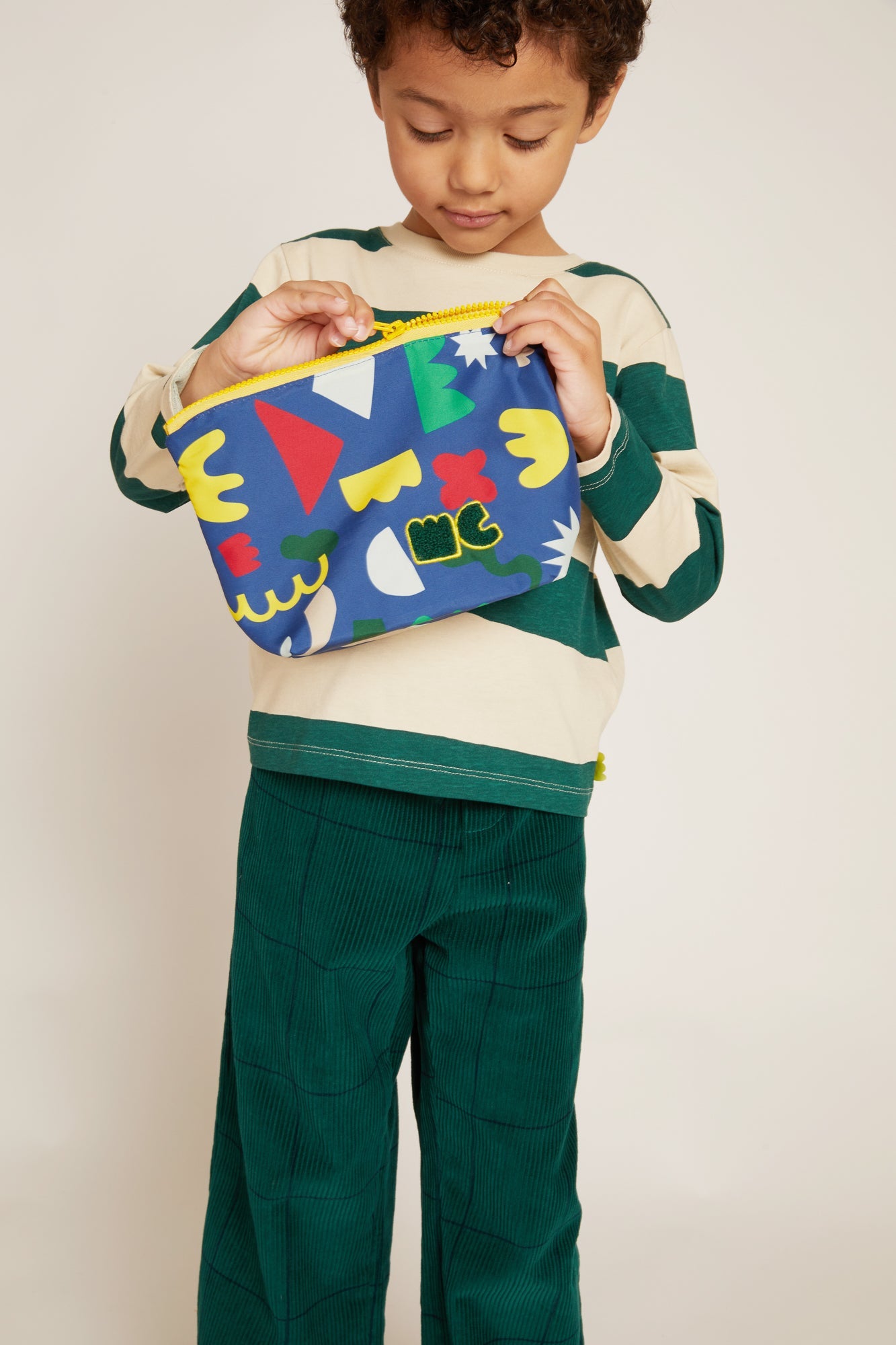 Child holding a colorful pouch with abstract designs on a plain background