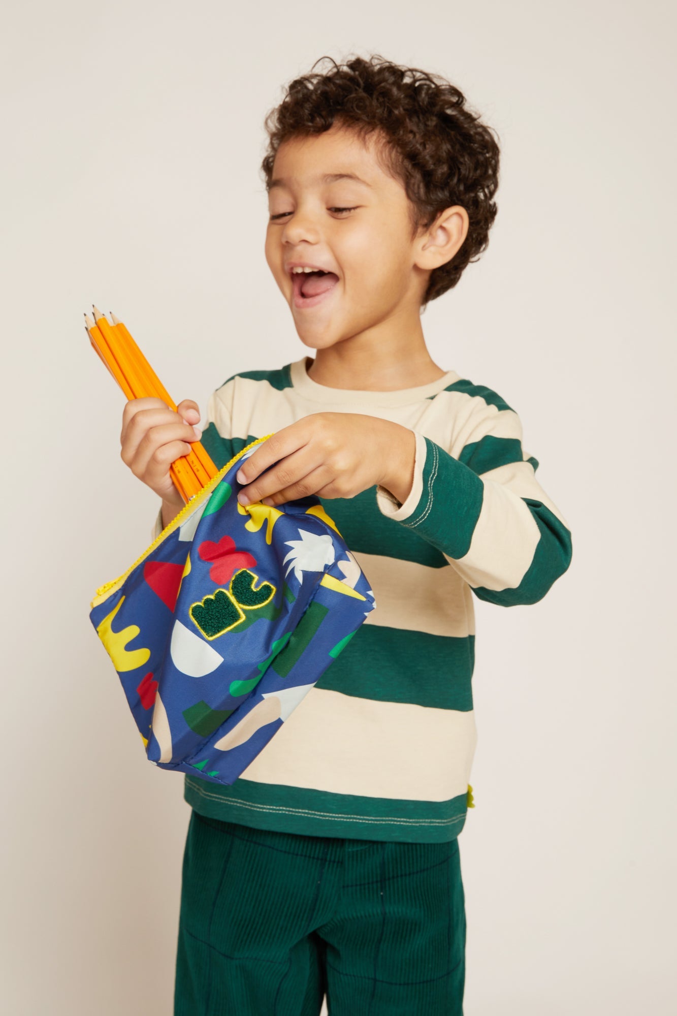 Child holding a colorful bag and pencils against a plain background