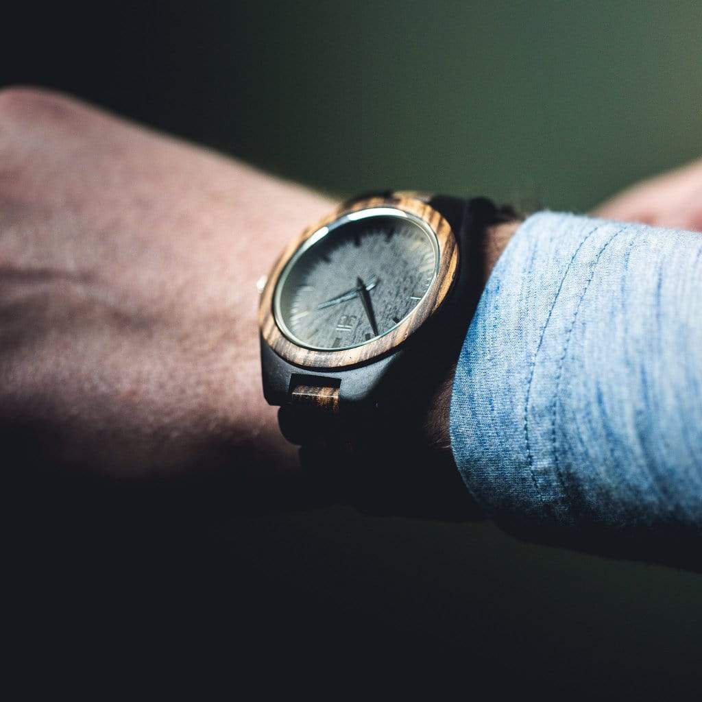 Wooden wristwatch on a person's wrist with a blurred background
