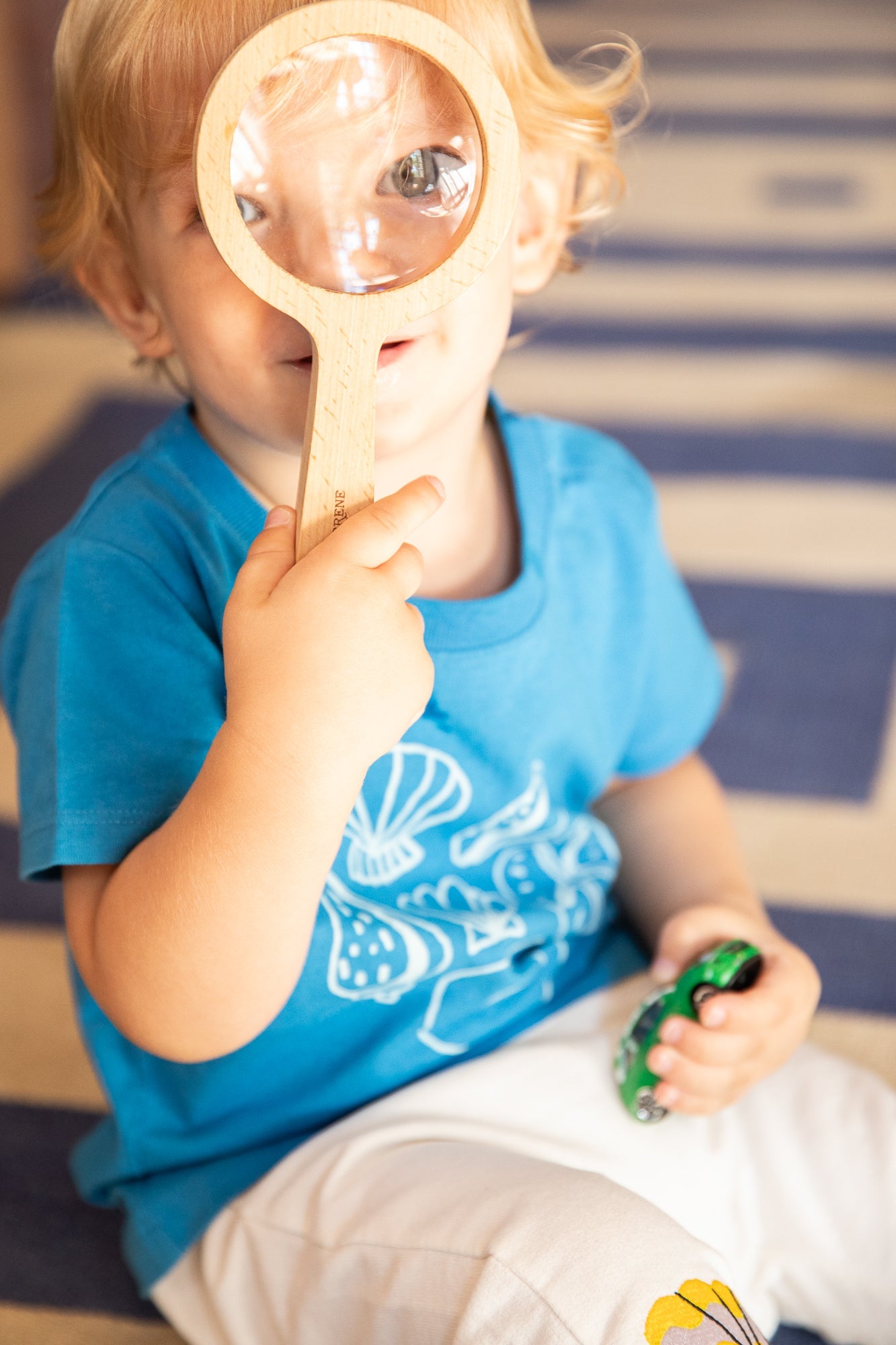 Child holding a magnifying glass up to their face with a striped background