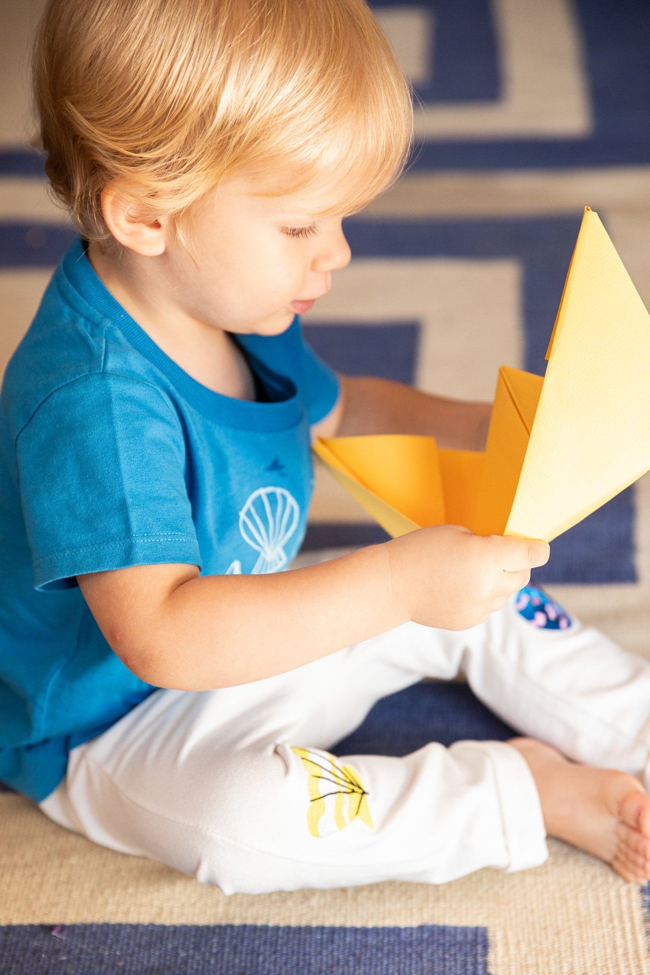 Child holding a yellow paper airplane on a patterned rug