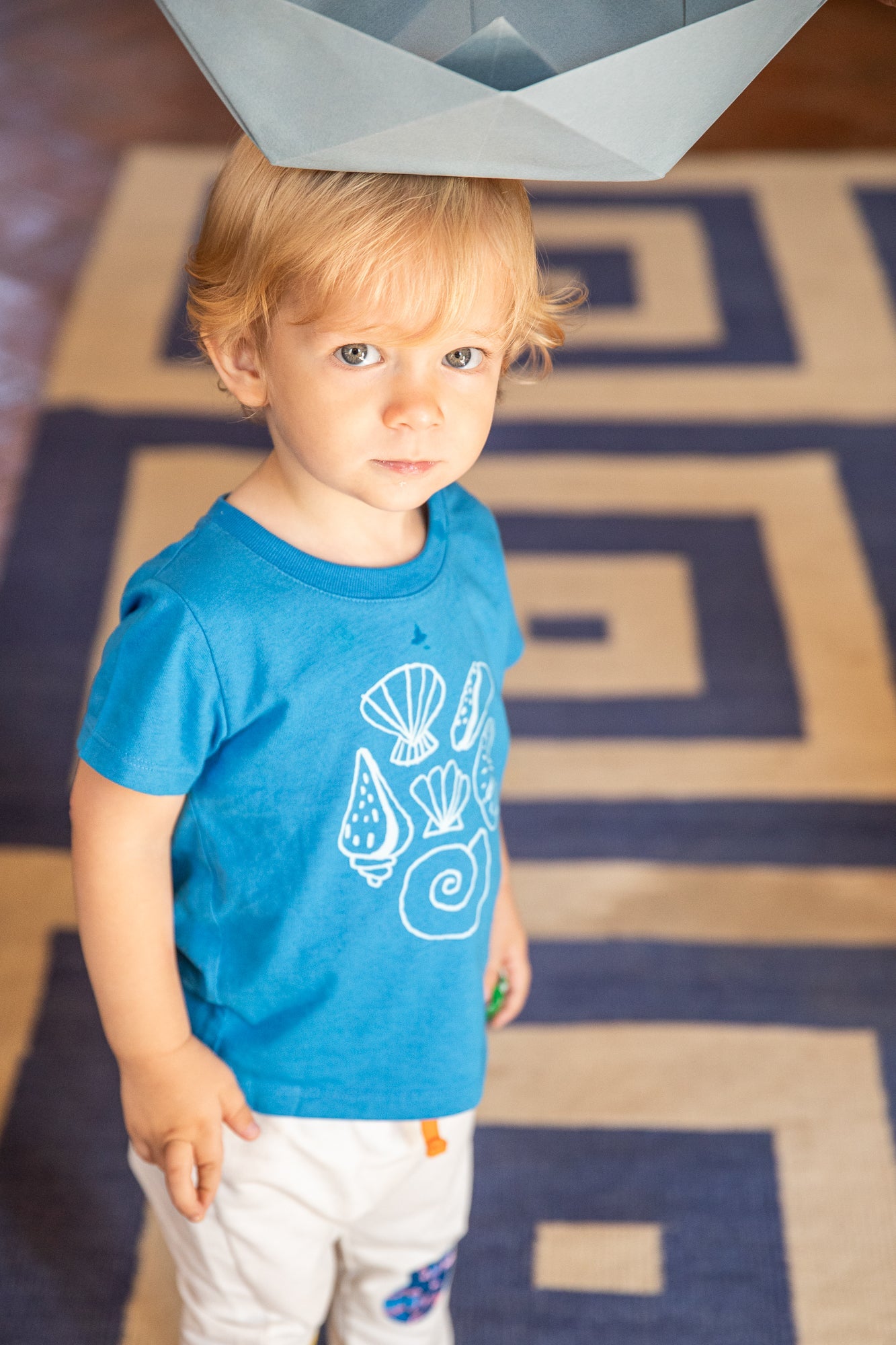 Child wearing a blue t-shirt with a graphic design, standing on a patterned rug.