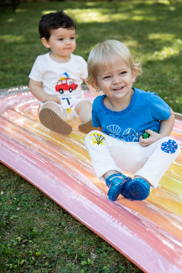 Two children playing on a colorful inflatable slide in a grassy area.