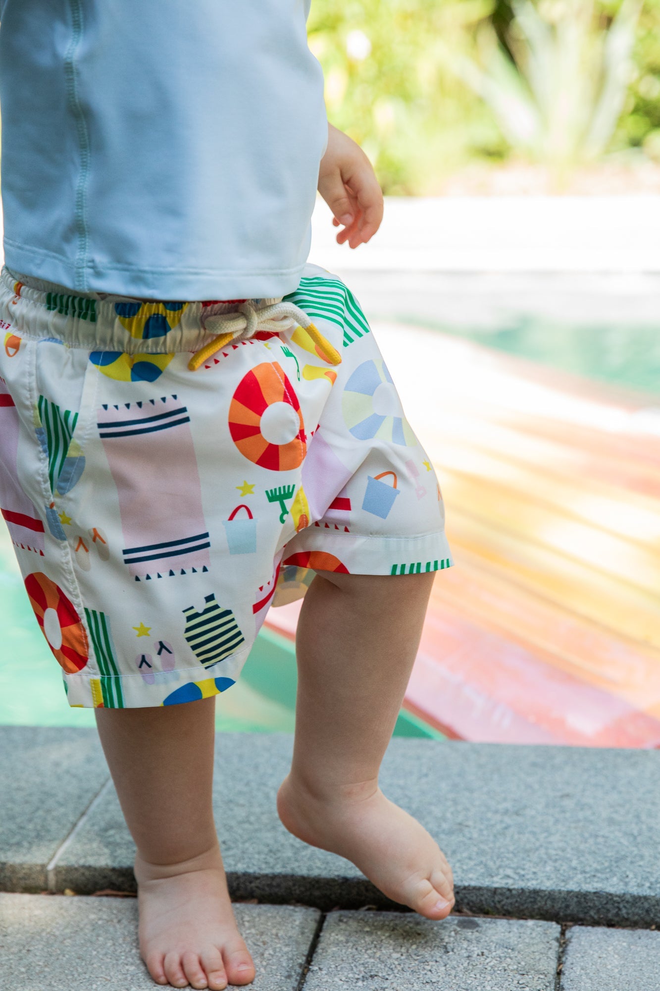 Child wearing colorful patterned shorts by a poolside
