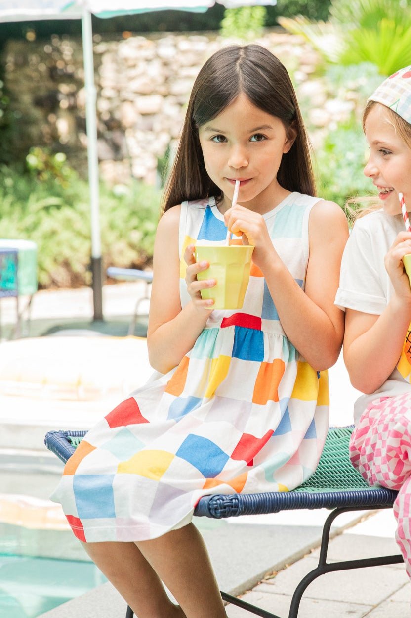 Two young girls sitting outdoors, drinking from colorful cups with straws.