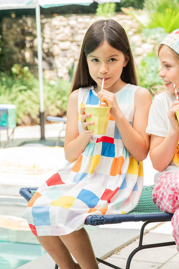 Two young girls sitting outdoors, drinking from colorful cups with straws.