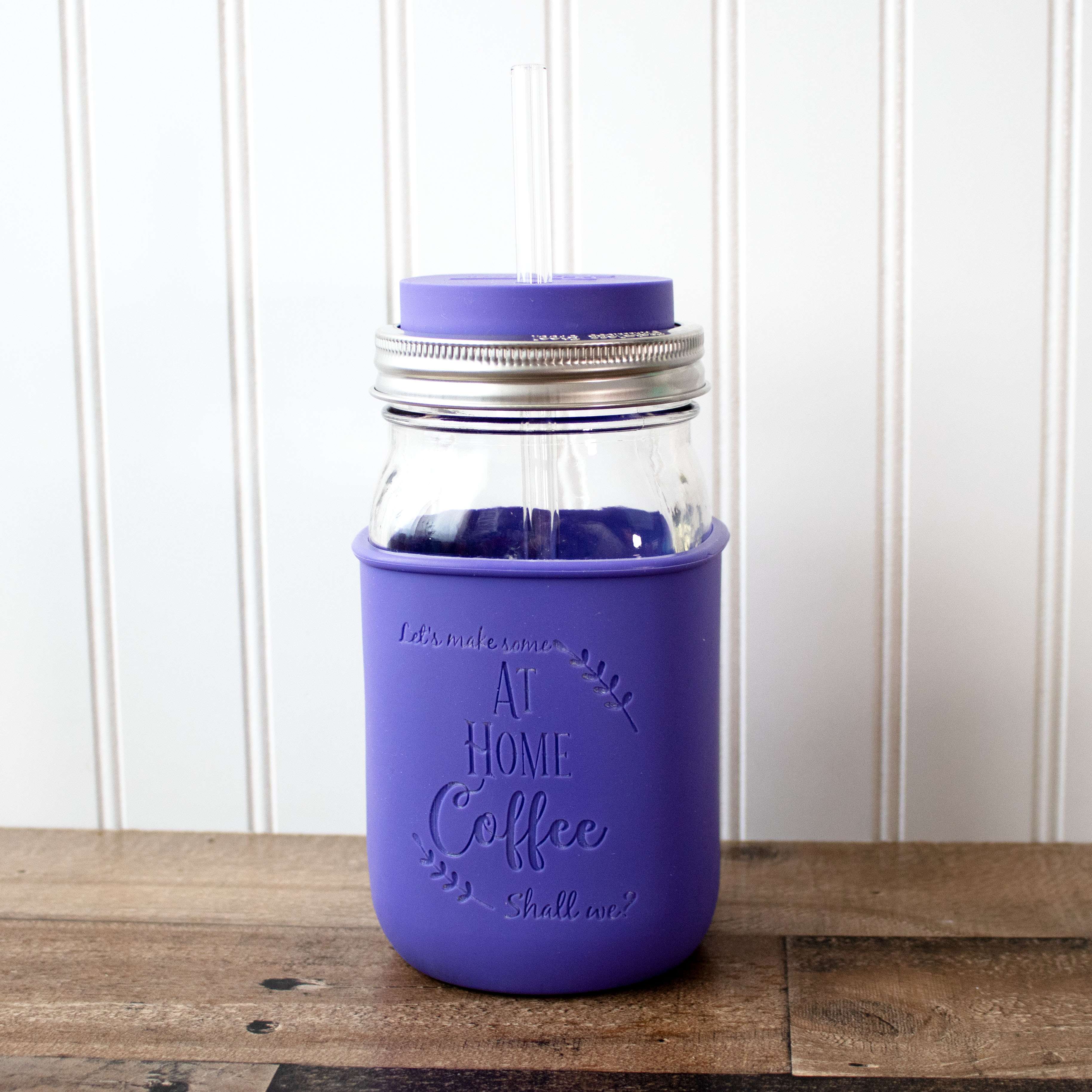 Purple insulated mug with a silver straw lid on a wooden surface.