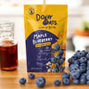 Dozy Oats Maple Blueberry Overnight Oats package with blueberries and syrup on a wooden surface