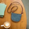 Blue handbag on a wooden table with a cup of coffee and books.
