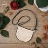 Beige handbag with black strap on a wooden surface with flowers and leaves.
