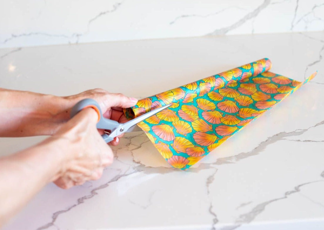Person cutting colorful paper with scissors on a marble surface