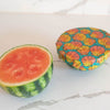 Half-cut watermelon next to a colorful shell-patterned container on a marble surface