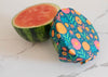 Half-cut watermelon next to a floral-patterned fruit cover on a marble surface