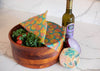 Wooden bowl with produce, a bottle of olive oil, and reusable food wraps on a marble surface.