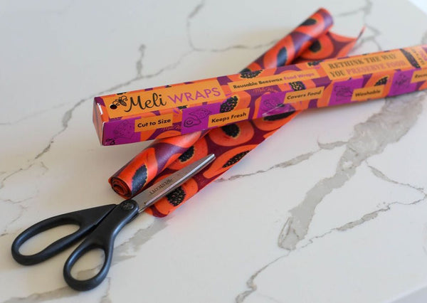 Meli Wraps packaging with orange and black design on a marble surface with scissors.