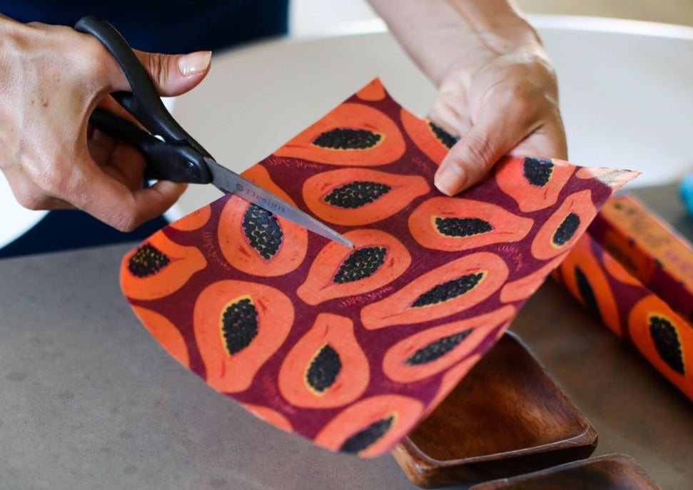 Person cutting a piece of paper with a papaya leaf pattern using scissors.