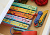 Colorful boxes of Meu Wraps on a wooden surface with colorful plastic items.
