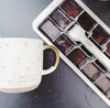Box of chocolates next to a mug with 'Morning Beautiful' text on a gray surface