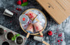 Ice cream popsicles with raspberry pieces in a bowl, surrounded by a box and kitchen tools on a dark surface.