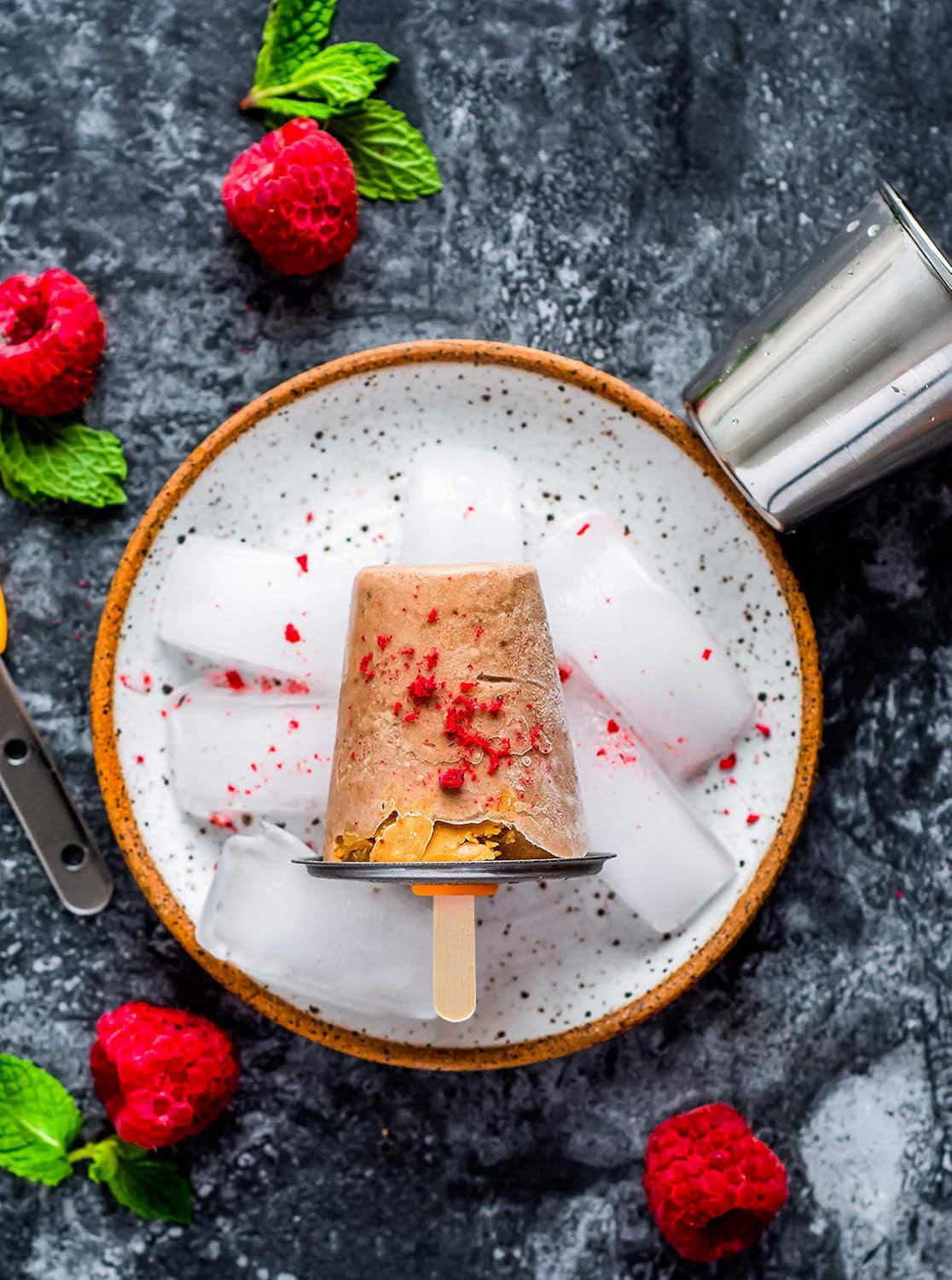 Popsicle on a bed of ice with raspberries and mint leaves on a dark surface