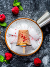 Popsicle on a bed of ice with raspberries and mint leaves on a dark surface
