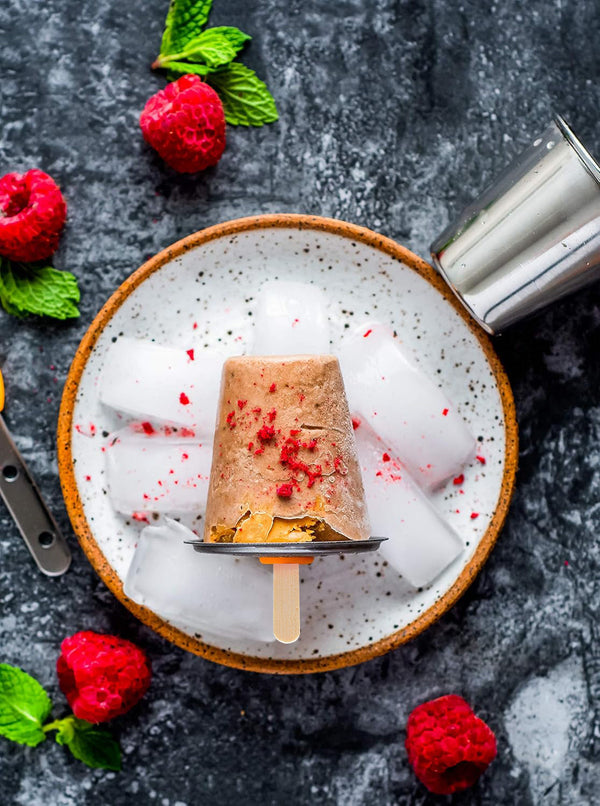 Popsicle on a bed of ice with raspberries and mint leaves on a dark surface
