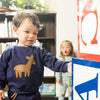 Child wearing a navy blue sweater with a deer design, standing next to a colorful sign.