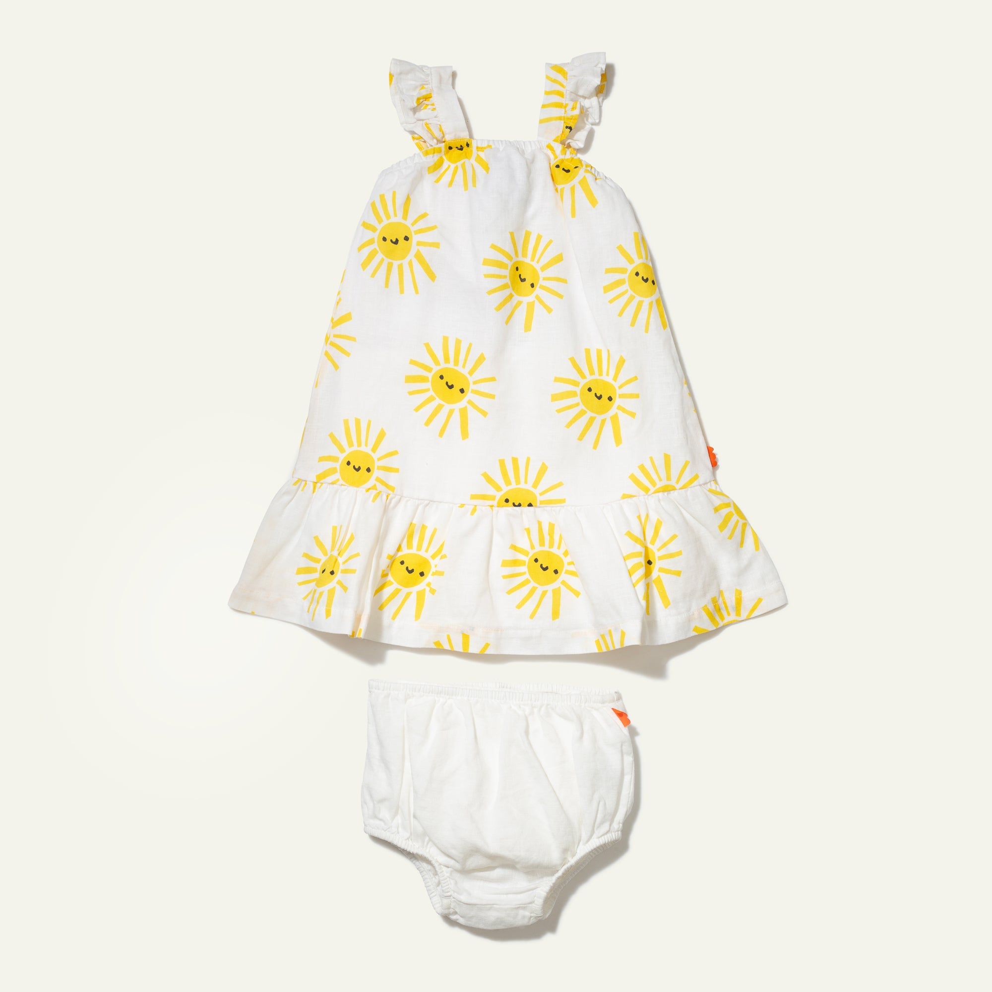 White baby dress with yellow sun patterns and white bloomers on a light beige background