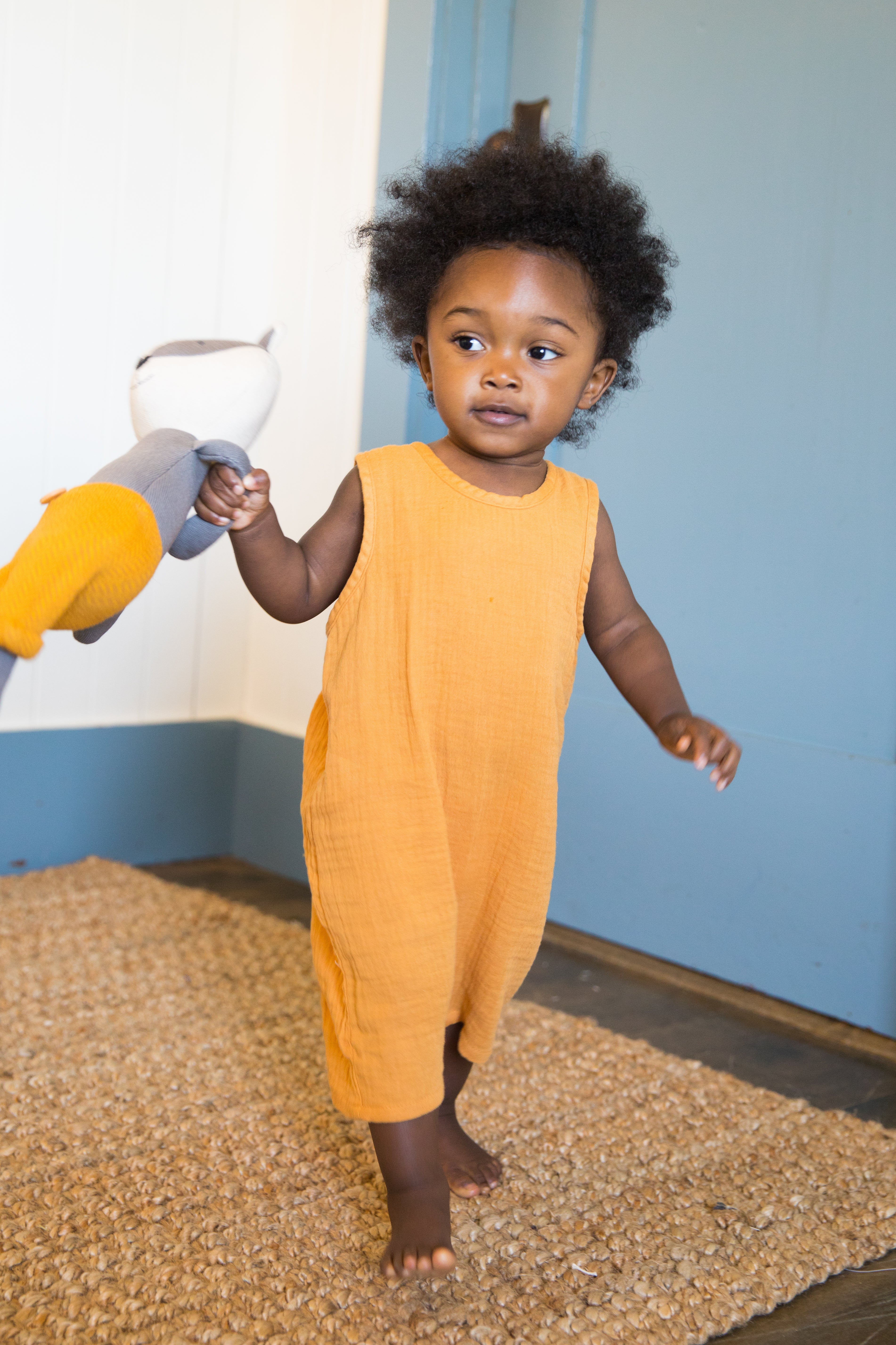 Close-up of mustard organic cotton muslin baby coverall with snap back neck closure