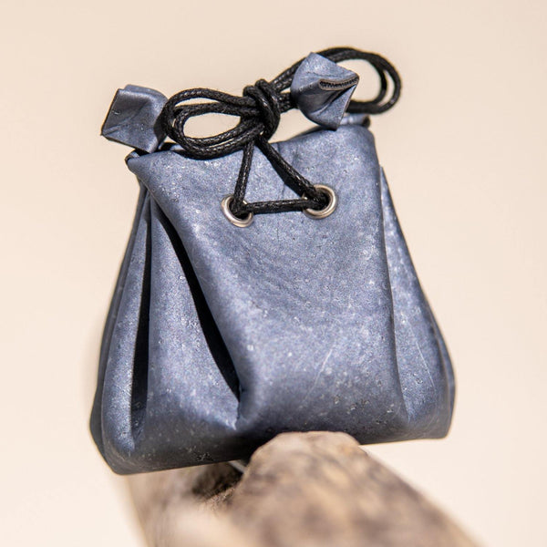 Small blue fabric pouch with a black drawstring on a beige background