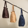 Three bags in brown, beige, and blue hanging on a branch against a neutral background