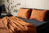 Orange pillows and blanket on a bed with a plant in the background