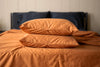 Orange pillows on a bed with orange bedding against a neutral wall.