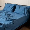 Blue bedding set on a bed in a room with a wooden floor and a plant.
