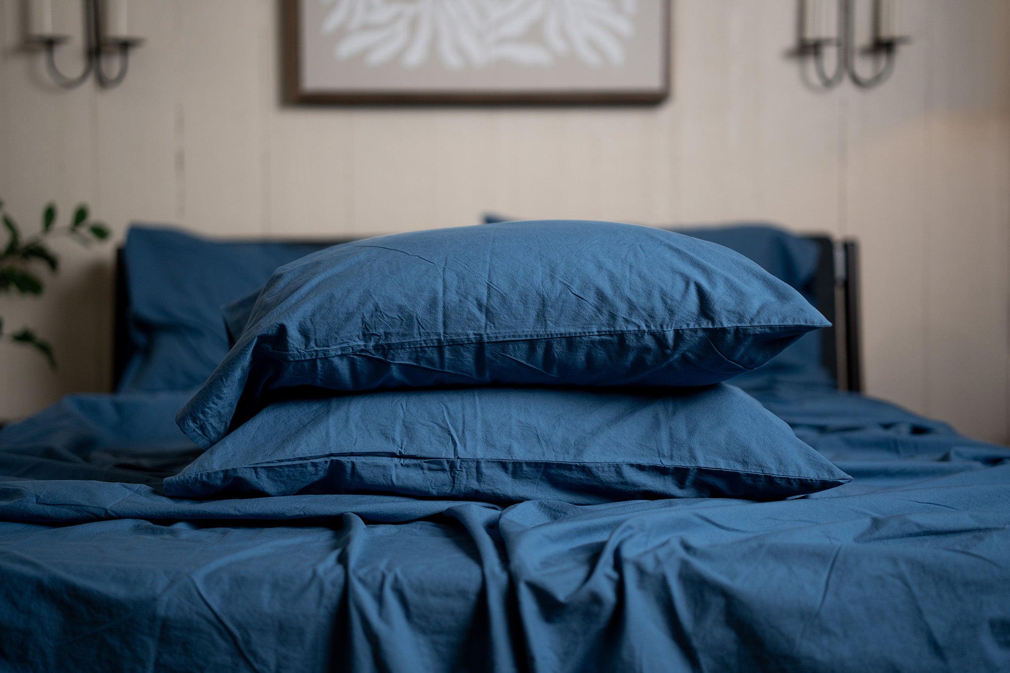 Blue bedding set on a bed with a neutral wall and plant in the background