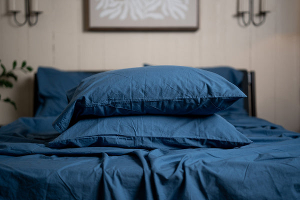 Blue bedding set on a bed with a neutral wall and plant in the background