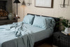 Bedroom with a bed featuring light blue bedding and pillows, nightstands with decorative items, and a lamp.