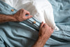 Person folding a light blue shirt with white buttons on a bed.