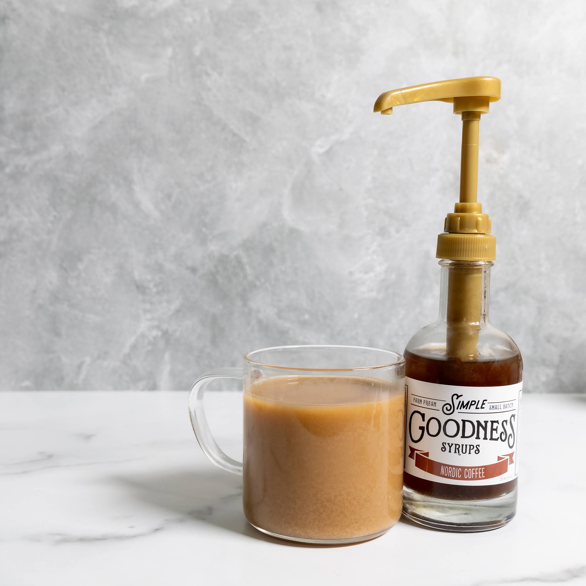 Bottle of Simple Goodness syrups next to a glass of coffee on a marble surface.