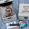 Wooden watch in a box with a branded card and sticker on a textured surface