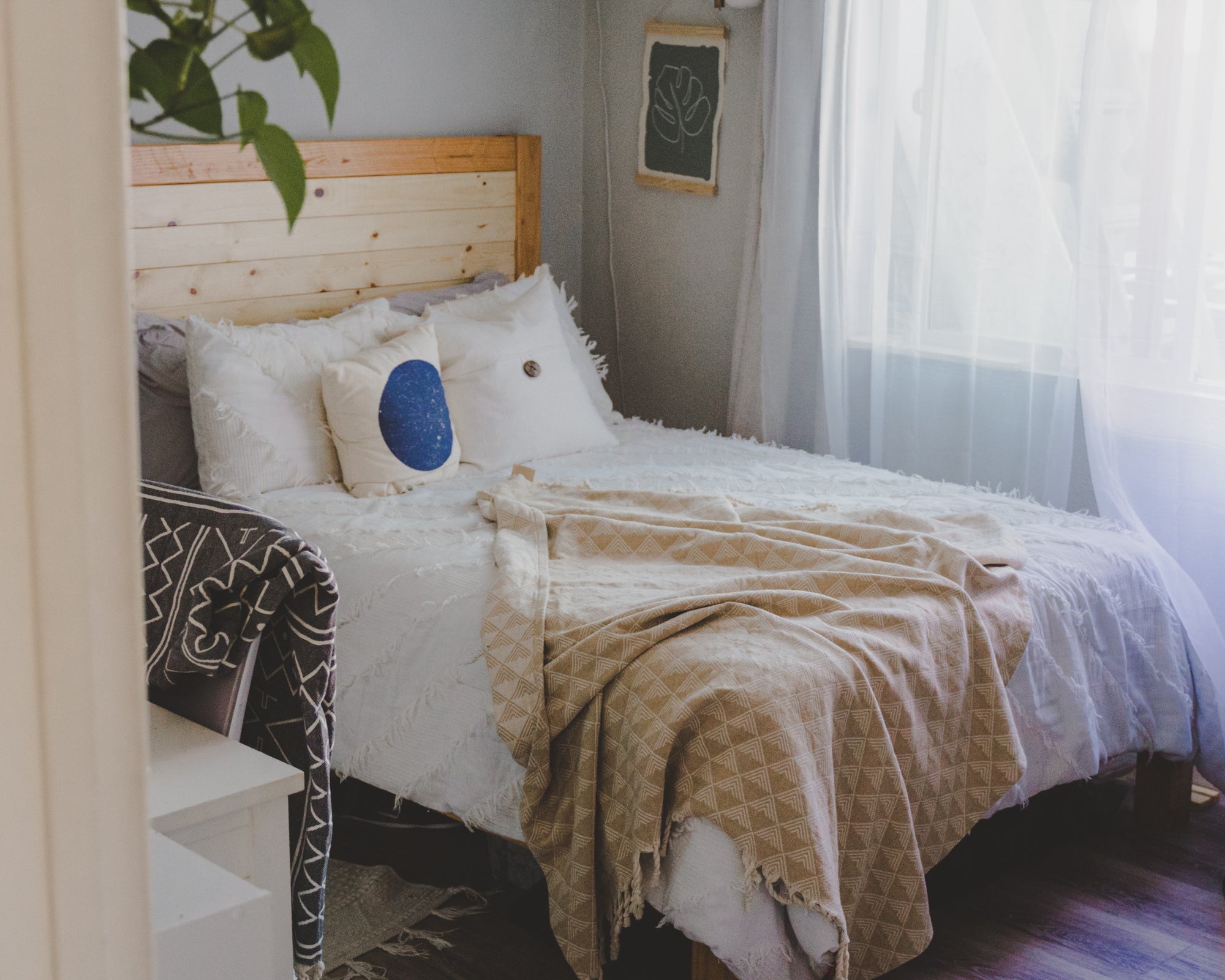 Bedroom with a bed featuring pillows and a blanket, next to a window with curtains.