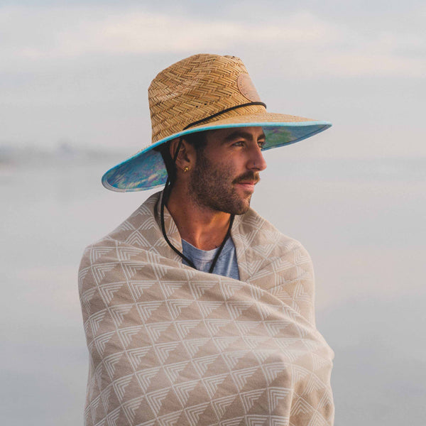 Man wearing a straw hat and wrapped in a patterned blanket against a blurred natural background