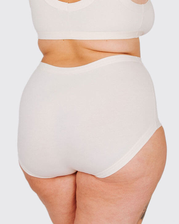 Person wearing a white high-waisted bikini bottom on a plain background