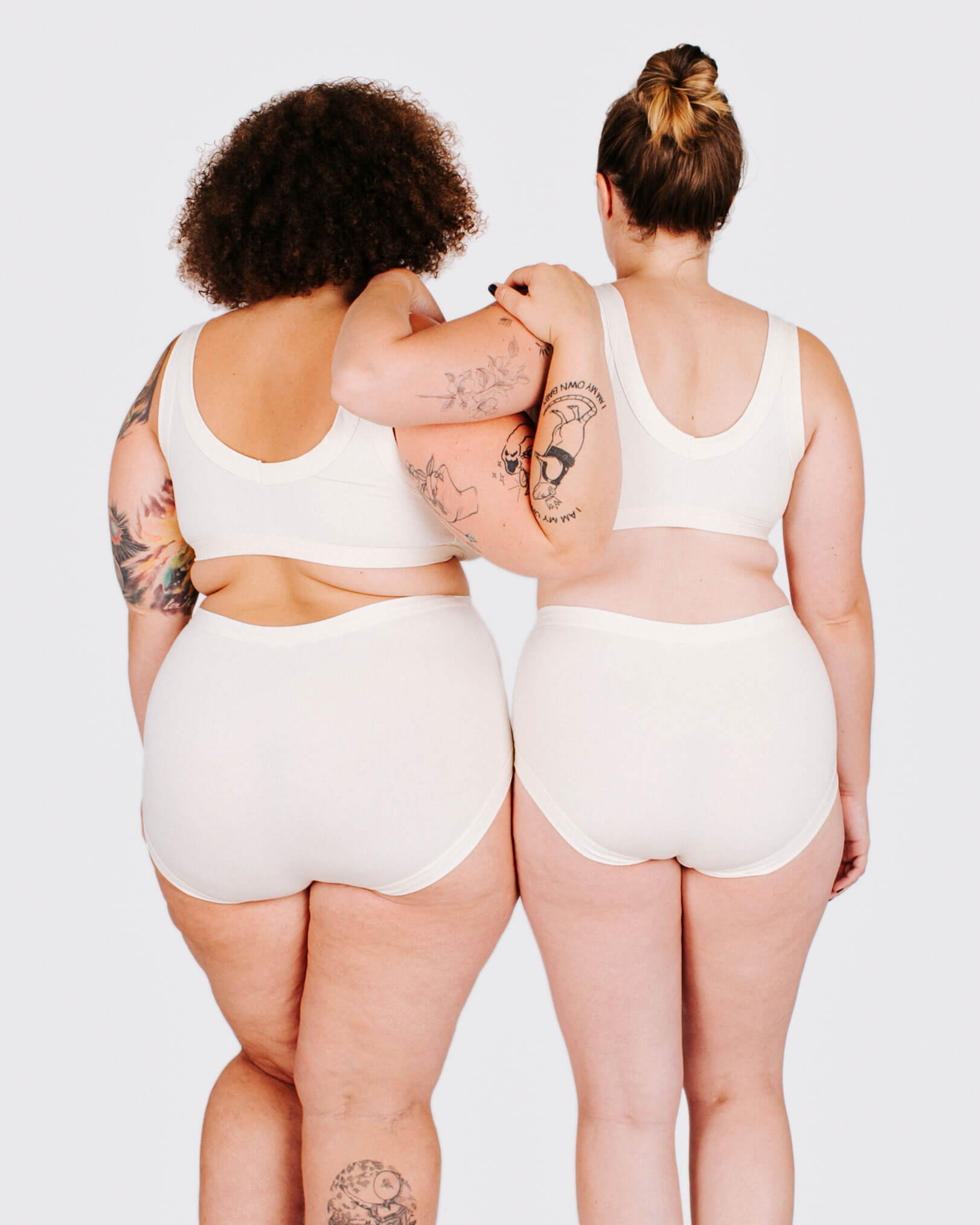 Two people wearing white tank tops and shorts from behind on a plain background
