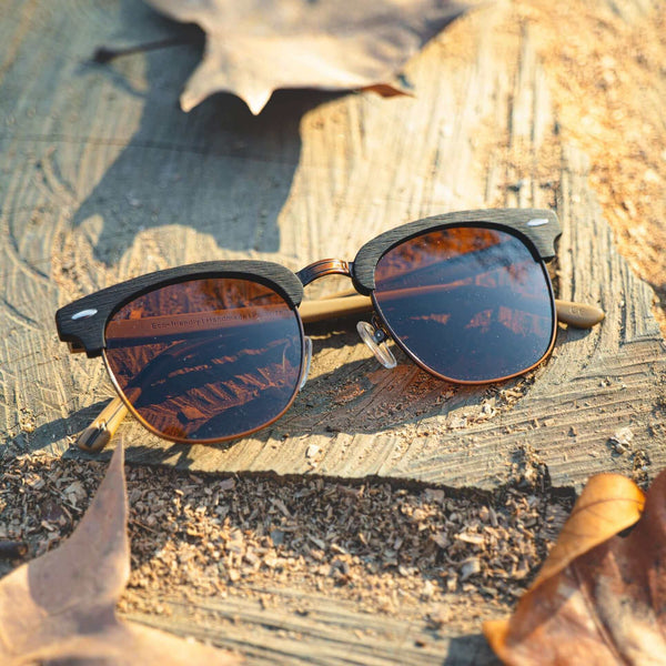 Sunglasses with reflective lenses on a wooden surface with leaves