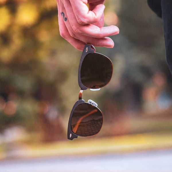 Sunglasses hanging from a person's hand with a blurred natural background