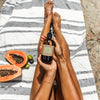 Person holding a bottle of Paavani Ayurvedic body oil with papaya and lime on a striped towel.