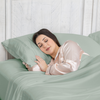 Woman sleeping peacefully in a bed with green bedding and pillow.